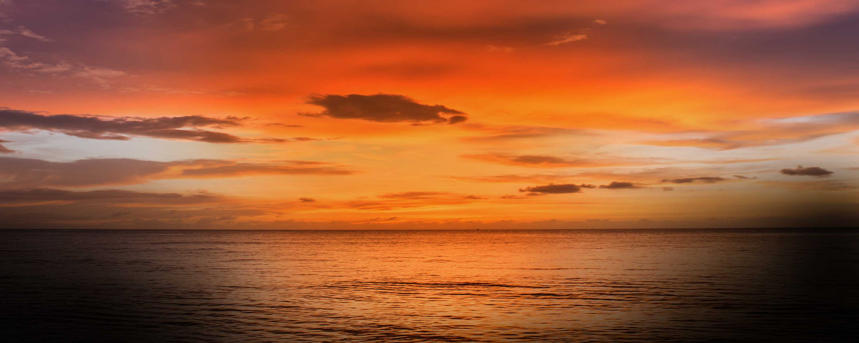 Vibrant orange sunset over calm sea with dramatic cloudy sky